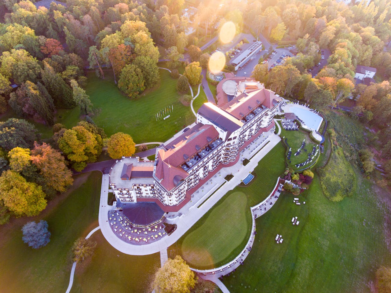 Grand aerial view of a luxurious hotel amidst vibrant autumn foliage, showcasing elegant architecture and expansive green grounds.